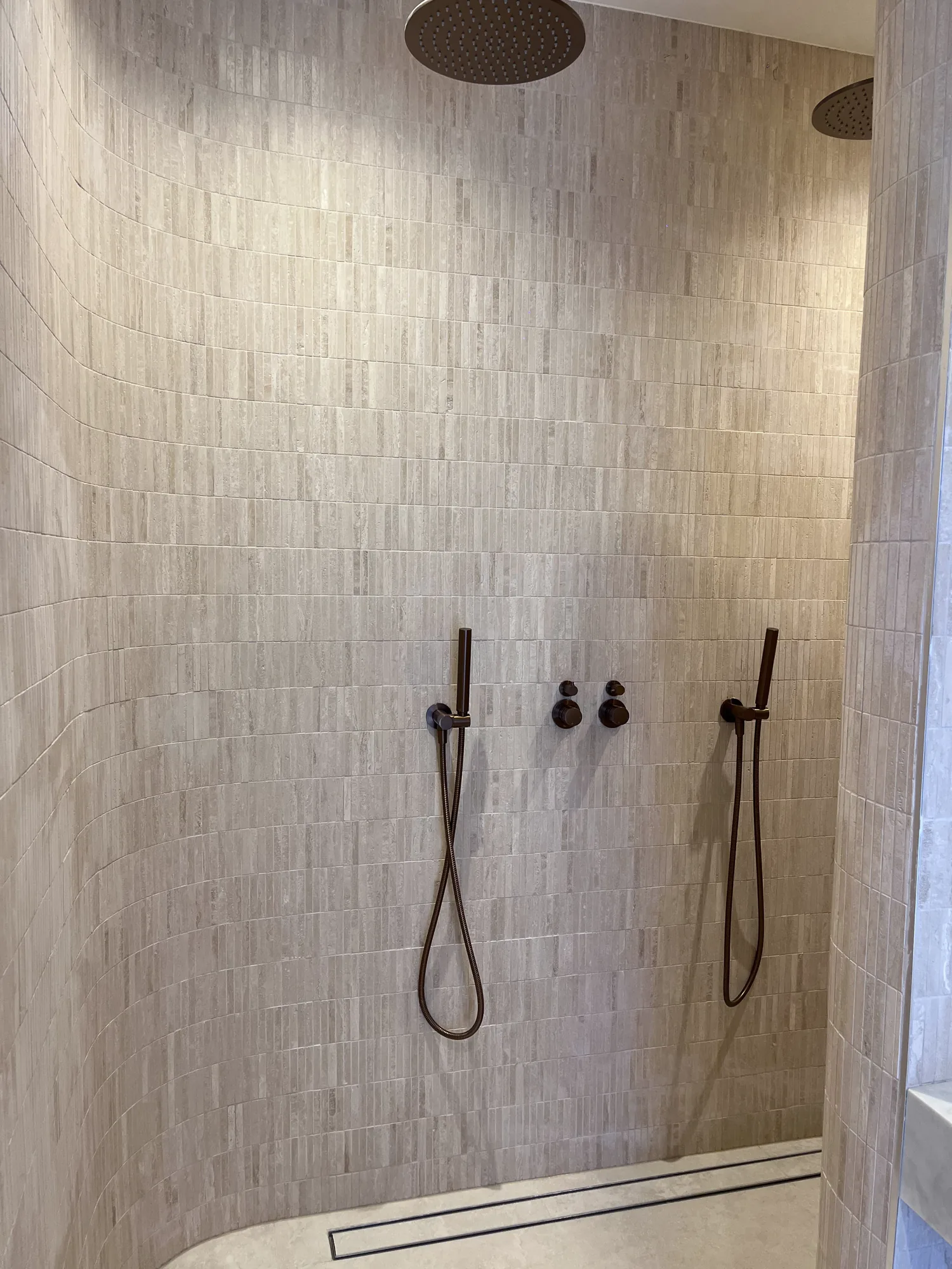 Full-height textured shower tiles with twin fittings and a linear drain.