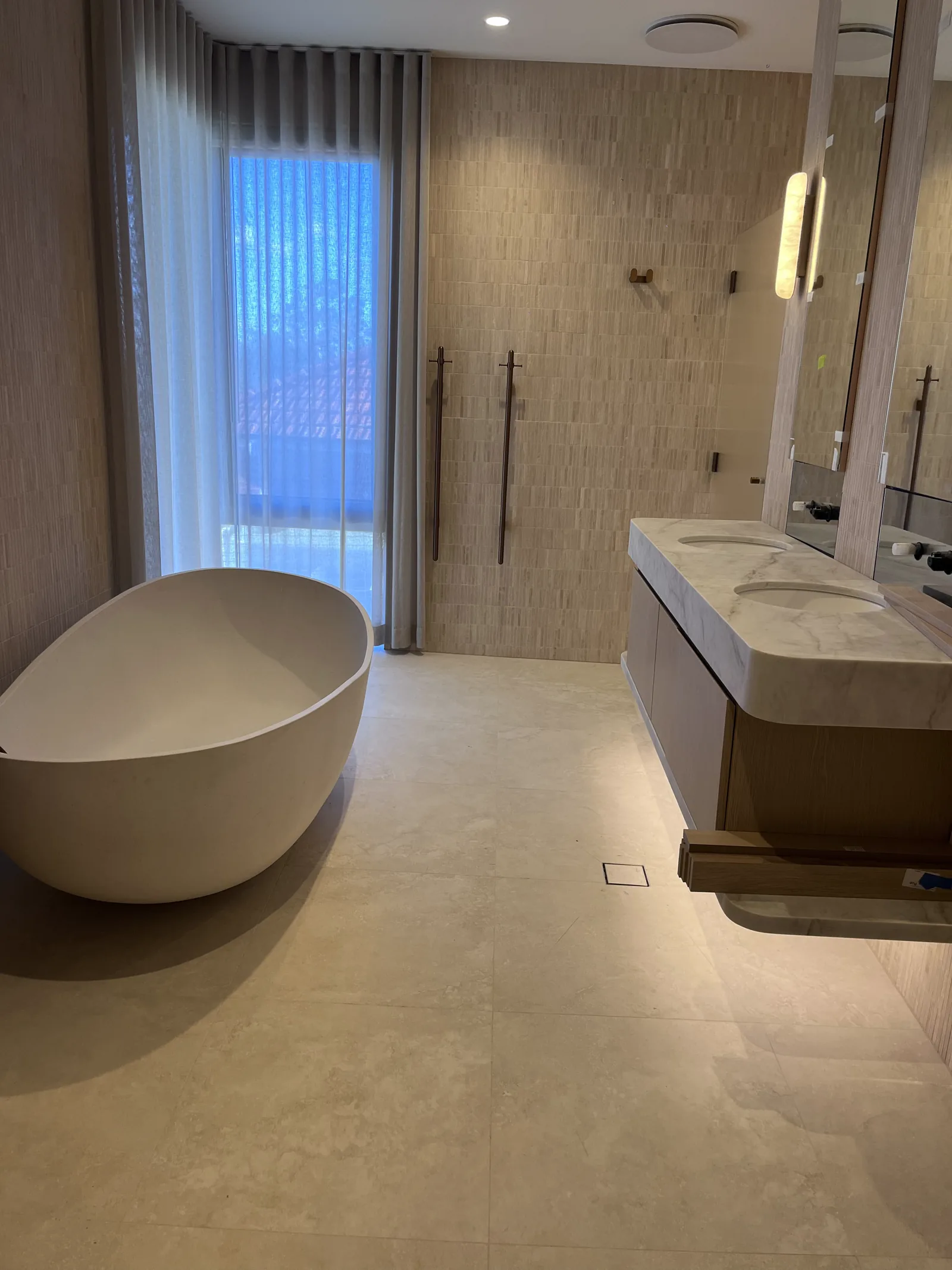 Finished warm-toned bathroom floor and full-height wall tiling around a freestanding bath.