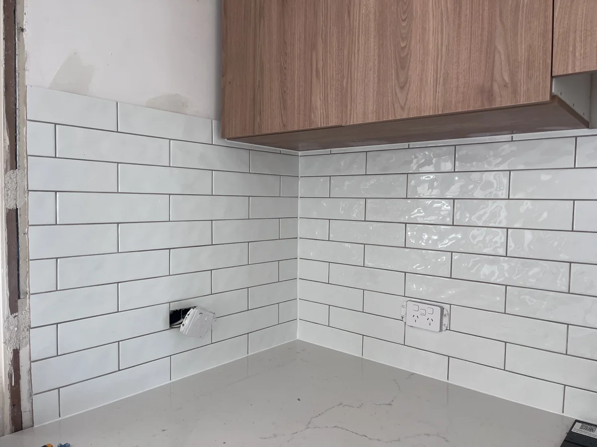 Glossy white subway splashback installed beneath timber kitchen cabinets.